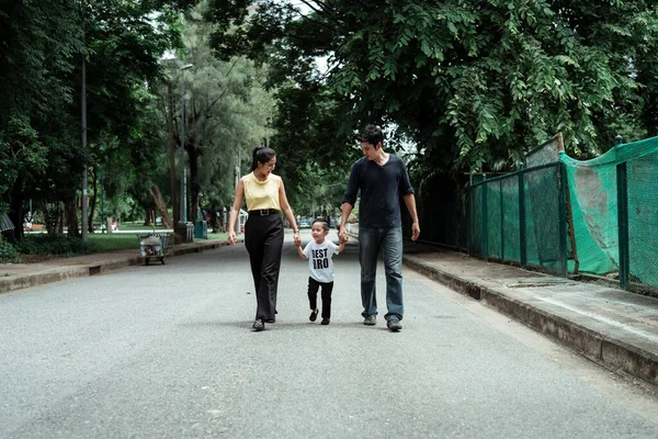 The family walking back home in the evening of weekend, the son holding parents\' hands whle walking.