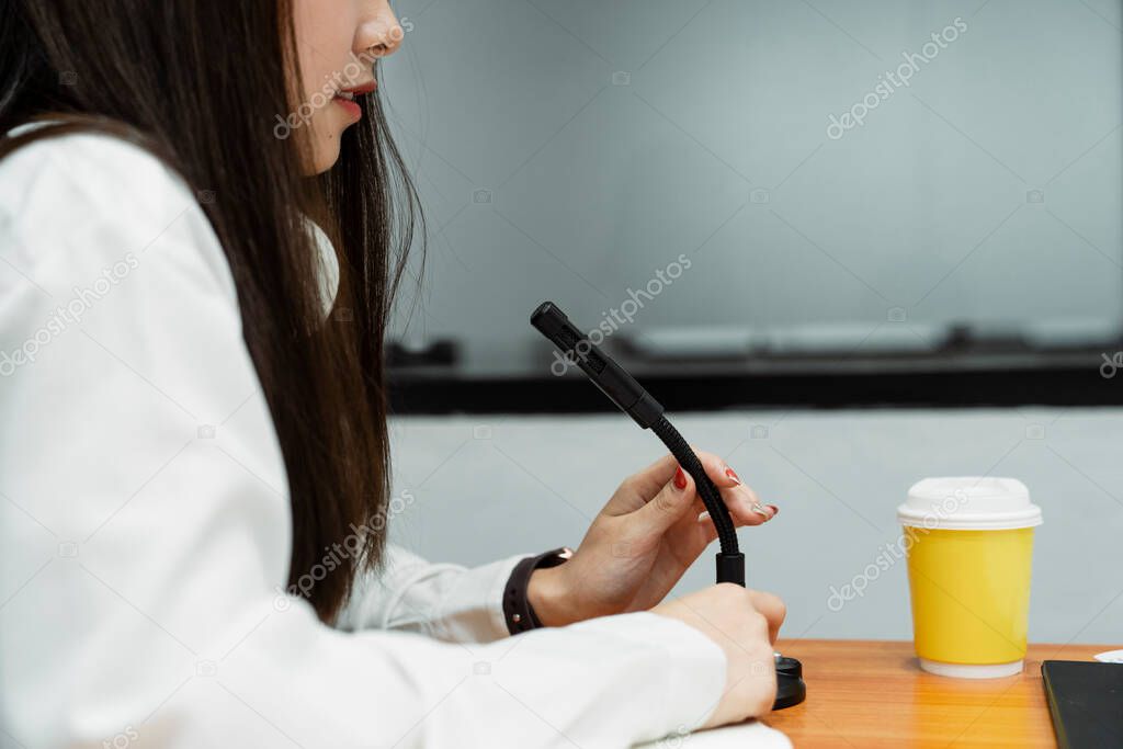 Cropped image of black microphone is held by woman podcaster on the wooden table with yellow cup of coffee.