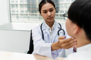 Kadın doktor erkek hastanın boğazına dokunuyor çünkü bademcik iltihabını düşünüyor..