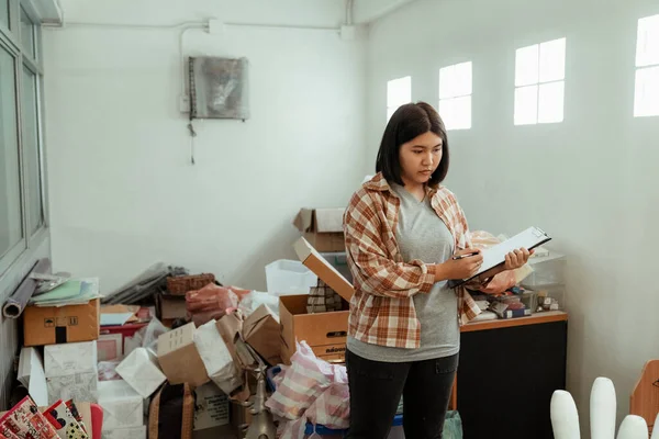 Woman handyman holding paper list of broken furniture and couting all stuff in warehouse.
