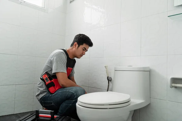 Tesisatçı adam oturup tuvaleti kontrol ediyor, sızıntı var mı diye. Asyalı tesisatçı tamir edilmesi gereken tuvaleti kontrol ediyor..