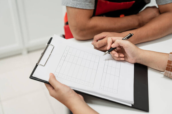 A hand of woman holding pen signing on white paper sheet which on clipboard.