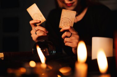Uzun saçlı güzel kadın falcı karanlık odada geleceği tahmin etmek için tarot kartını kullanıyor..