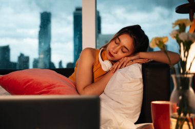 Kulaklıkla müzik dinlerken kanepede uyuyan güzel melez bir kadın..