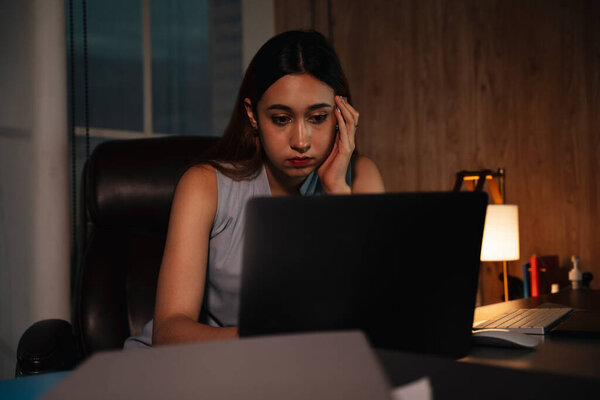 Женщина смешанных рас работает по ночам за ноутбуком.