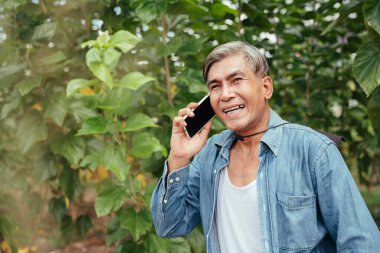Çiftlikte çalışırken akıllı telefon kullanan Asyalı yaşlı çiftçi.