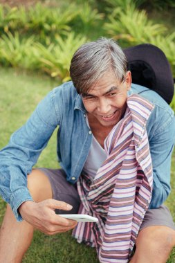 Neşeli Asyalı yaşlı çiftçi çiftlikte akıllı telefon kullanıyor..