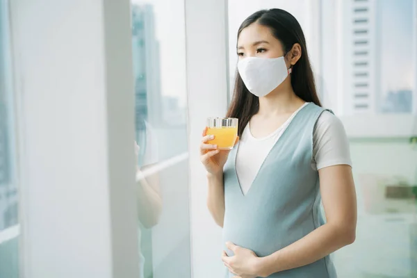 Vacker Gravid Asiatisk Kvinna Bär Bomullsmask Håller Glas Apelsinjuice Hemma — Stockfoto