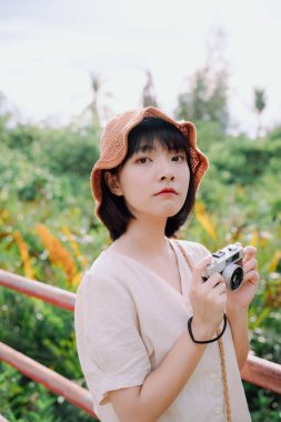 Güzel Asyalı Taylandlı kadın. Kısa siyah saçlı fotoğrafçı. Doğada film kamerasıyla fotoğraf çekiyor..