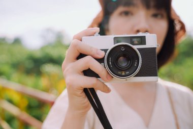 Yakın çekim - güzel Asyalı Taylandlı kadın, kısa siyah saçlı, klasik kamerayı doğada tutuyor. Güzel fotoğrafçı..