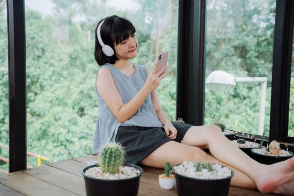 在当地仙人掌农舍 美丽的亚洲女人喜欢用无线耳机和智能手机听音乐 — 图库照片