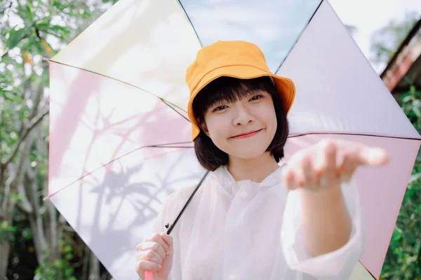 时尚肖像 美丽的亚洲女人 深色短发 穿着白色外套 头戴黄色帽子 在雨季拿着彩霞雨伞 — 图库照片