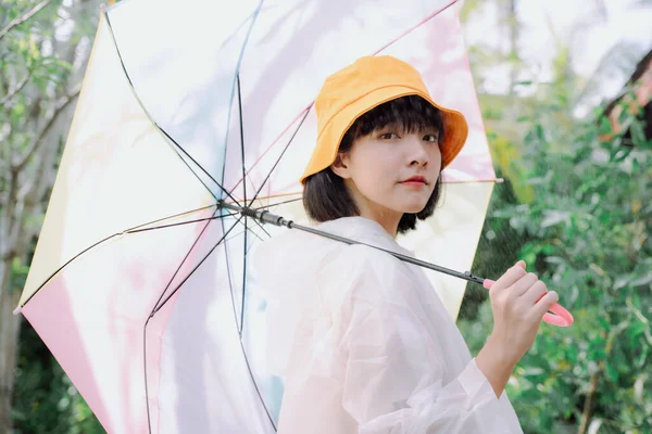 아름다운 아시안 장마철에 파스텔 무지개 우산을 코트와 노란색 모자를 — 스톡 사진