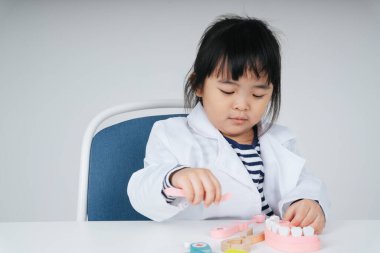 Güzel Asyalı Taylandlı çocuk diş fırçasıyla dişlerini fırçalayan bir dişçi rolü oynuyor..