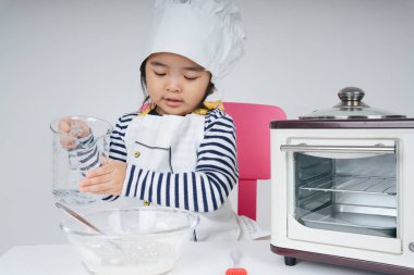 Tatlı Asyalı Taylandlı çocuk mutfakta karıştırma kabına su döken bir şef rolünde oynuyor..
