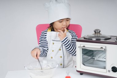 Tatlı Asyalı Taylandlı çocuk fırında pişirmeden önce un ve suyu cam kaseye karıştırarak şef rolü oynuyor..