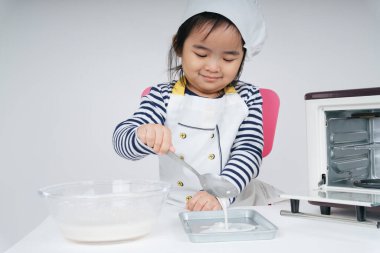 Tatlı Asyalı Taylandlı çocuk aşçı rolünde oynuyor. Fırın tabağına karışık un koyuyor.