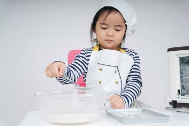 Tatlı Asyalı Taylandlı çocuk aşçı rolünde oynuyor. Fırın tabağına karışık un koyuyor.