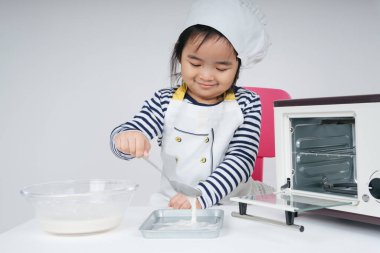 Tatlı Asyalı Taylandlı çocuk aşçı rolünde oynuyor. Fırın tabağına karışık un koyuyor.