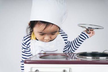 Güzel Asyalı Taylandlı çocuk fırınlı yemek pişirme istasyonunda şef rolünde oynuyor..