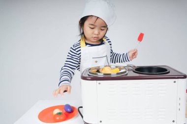 Güzel Asyalı Taylandlı çocuk mutfakta sarı bandajlı aşçı rolünde oynuyor..