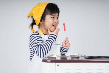Güzel Asyalı Taylandlı çocuk, mutfakta ocakla yemek pişiren sarı bandajlı bir şef rolünde oynuyor..
