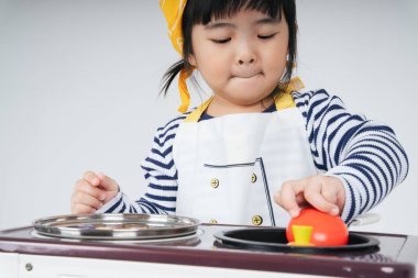 Güzel Asyalı Taylandlı çocuk, mutfakta ocakla yemek pişiren sarı bandajlı bir şef rolünde oynuyor..