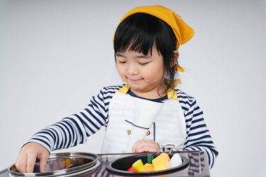 Güzel Asyalı Taylandlı çocuk, mutfakta ocakla yemek pişiren sarı bandajlı bir şef rolünde oynuyor..