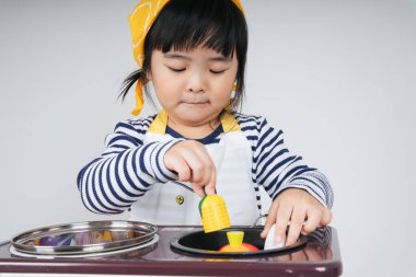 Güzel Asyalı Taylandlı çocuk, mutfakta ocakla yemek pişiren sarı bandajlı bir şef rolünde oynuyor..