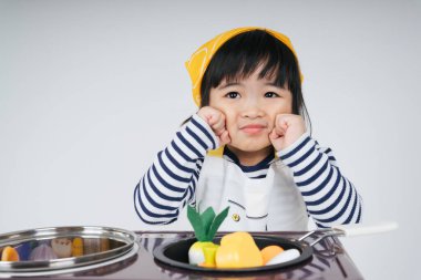 Güzel Asyalı Taylandlı çocuk mutfakta fırınlı sarı bandaj giyen bir şef rolünde oynuyor..