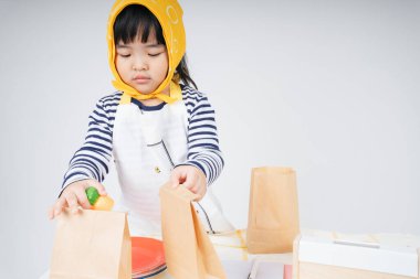 Güzel Asyalı Taylandlı çocuk, sarı bandajlı garsonluk yapıyor ve kese kağıdına yemek dolduruyor..