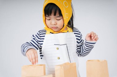 Güzel Asyalı Taylandlı çocuk, sarı bandajlı garsonluk yapıyor ve kese kağıdına yemek dolduruyor..