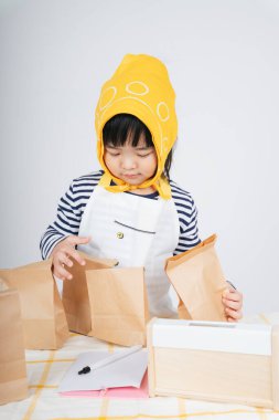 Güzel Asyalı Taylandlı çocuk, sarı bandajlı garsonluk yapıyor ve kese kağıdına yemek dolduruyor..