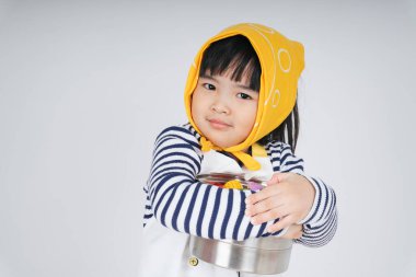 Güzel Asyalı Taylandlı çocuk, garsonluk yapıyor. Sarı bandaj takıyor, tencereye sarılıyor, beyaz arka planda soyutlanıyor..