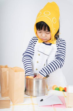 Güzel Asyalı Taylandlı çocuk, tencerede yemek pişiren sarı bandajlı garson rolünü oynuyor..