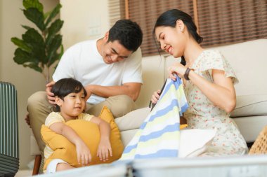Asyalı thai ailesi evde iyi vakit geçiriyor. Aile eşyalarını bavula koy. Yolculuğa hazırlanın..