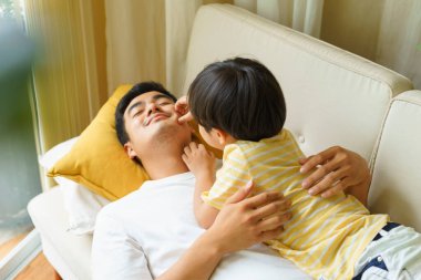 Asyalı Taylandlı baba ve oğlu evde birlikte eğleniyorlar. Oyuncu çocuk baba yüzüyle oynuyor..