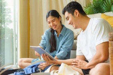 Asyalı Tayland ailesi otel ve uçuş işlemlerini dijital dizüstü bilgisayarla yapıyor. Bagajda birkaç eşya var..