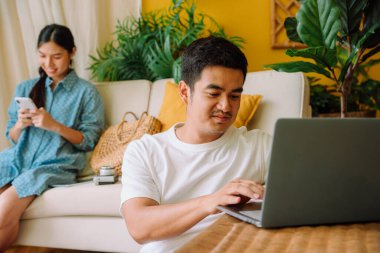 Yetişkin Asyalı bir adam laptop kullanarak otel odası rezervasyonu yapıyor ve web sitesinde bilgisayar laptopuyla uçuyor..