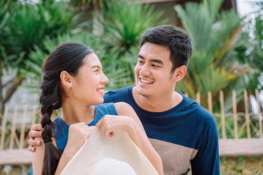 Neşeli ve heyecanlı Asyalı Taylandlı çiftler birbirlerine gülümsüyor. Adam arkadan kadına sarılıyor..