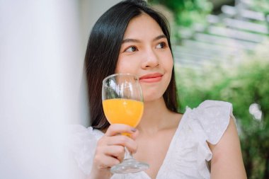 Güzel Asyalı Taylandlı kadını yakından çek. Uzun siyah saçlı, beyaz gömlekli. Sağlıklı portakal suyu iç.