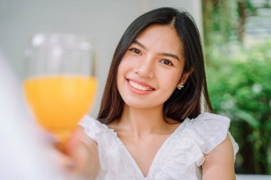 Güzel Asyalı Taylandlı kadını yakından çek. Uzun siyah saçlı, beyaz gömlekli. Sağlıklı portakal suyu iç.