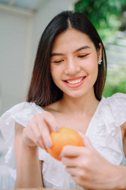 Güzel Asyalı, uzun siyah saçlı, beyaz gömlekli, turuncu meyveli bir kadının portresini yakından çek..