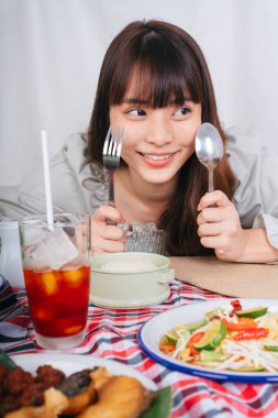 Isan yemeği ve Tayland çayıyla çatal bıçak tutan Asyalı kadının portresi..