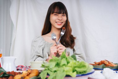Evde çatal ve kaşıkla Isan yemeği yiyen Asyalı kadın portresi.