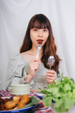 Evde çatal ve kaşıkla Isan yemeği yiyen Asyalı kadın portresi.