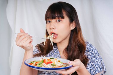 Papaya salatası ve çatallı yemek yiyen Asyalı genç bir kadının portresi..
