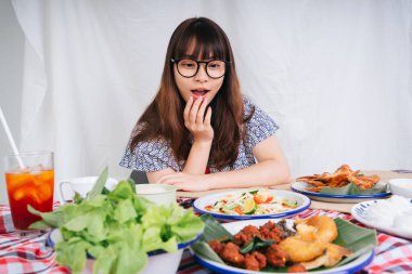 Gözlüklü genç Asyalı kadının portresi masada Isan yemeklerine şaşkın bir ifadeyle bakıyor..