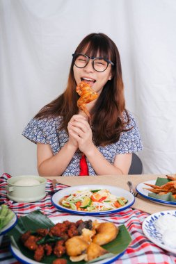 Mutlu bir ifadeyle kızarmış tavuk kanadı yiyen Asyalı genç kadının neşeli portresi..