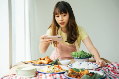 Genç Asyalı kadının portresi evde akıllı telefonla Isan yemeklerini çekiyor..